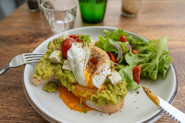 Sourdough toast, poached eggs, avocado pulp and fresh vegetables on plate in cafe, close up