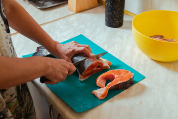 Hand cutting raw headless salmon fish laying on blue cutting board at home
