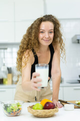 beautiful healthy woman show milk in glass, smile, happy, look at camera in kitchen. beautiful caucasian woman cooking healthy diet fruit or vegetable in kitchen