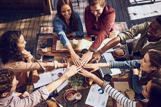 Because teams who eat together, stay together. High angle shot of a group of creative workers piling their hands while out on a business lunch.