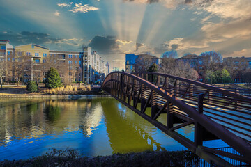 a long rust colored iron bridge over a rippling green lake in the park surrounded by apartment...
