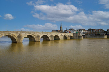 Maastricht (Sint Servaasbrug), Netherlands - February 13. 2022: View over river maas on old arched limestone pedestrian bridge against blue winter sky