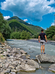 A man watching the black (shavi) Aragvi river and white (tetri) Aragvi river in Georgia that do not mix up. Unmixed waters. Confluence of rivers, Caucasus Mountains. Georgian military Highway.