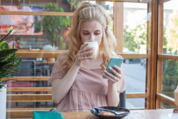 Young cute woman sitting at a table with a coffee using mobile phone.