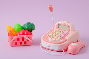 play store, children's toy cash register and basket of vegetables on lilac background, food...