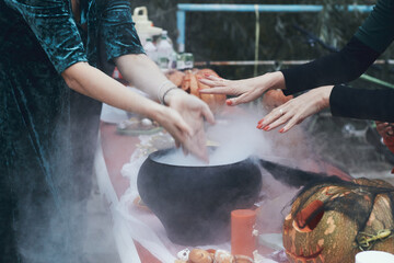 Many hand put near the smoking cauldron during halloween celebration