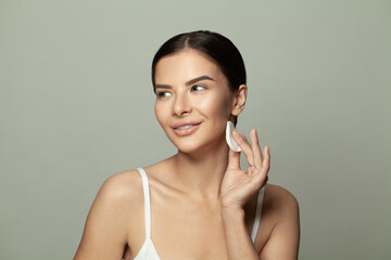 Happy woman cleaning her face with cotton pads and looking aside on white background