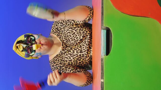 A Jewish woman in a headdress and a carnival mask commands when to make noise in the synagogue on Purim while shaking a rattle while reading a scroll
