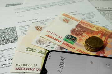 Комунальные платежи.Российские деньги,смартфон с включенным  калькулятором лежат на квитанциях по ЖКХ