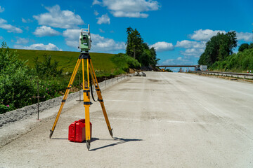 Surveyors equipment (theodolite or total positioning station) on the construction site of the road, highway or building with construction machinery background