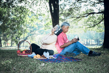 Asian elderly couple, attractive wife and husband, picnic and relaxing on the green lawn in garden, are smile and happy together, to relationship of retirement age and nature concept.