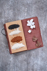 Notebook for recipes with cooking ingredients: sugar, cacao, flour of wheat and coconut on a gray grunge background. Selective focus