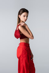 young woman in red outfit holding stylish bag isolated on grey.