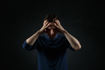 Emotional portrait of a man holding his head with his hands on a dark background.