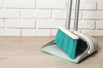 Plastic broom with dustpan near white brick wall indoors. Space for text