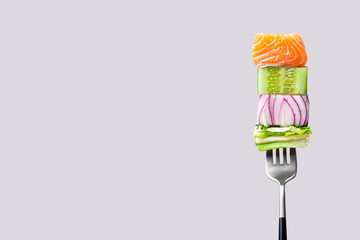 Close-up of fork with food on it: delicious fillet salmon, cucumber, onion, green salad on gray...