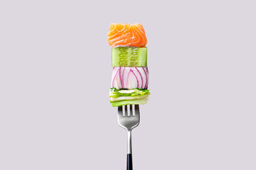 Close-up of fork with food on it: delicious fillet salmon, cucumber, onion, green salad on gray...