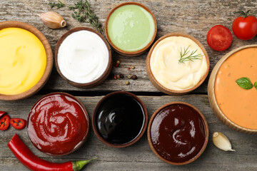Many different sauces on wooden table, flat lay