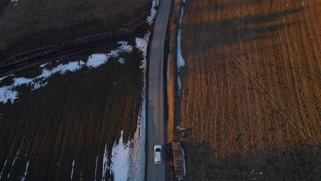 A moving car along a road leading through a rural landscape going to the horizon with forests and poly at sunset