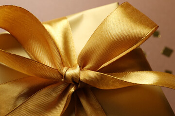 Beautiful golden gift box with bow on brown background, closeup