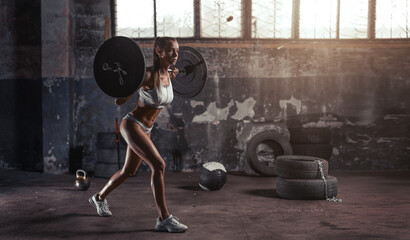 Sexy woman with muscular body training legs in old garage. lunges using barbell.