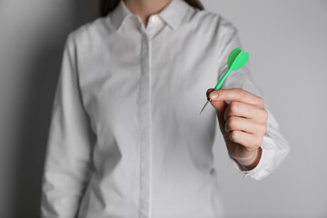 Businesswoman holding green dart on light background, closeup