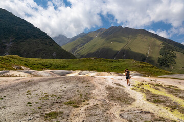 Fototapeta premium A woman walking on colorful mineral springs on ground in Truso Gorge in Kazbegi district, Mtskheta-Mtianeti region, Georgia. Truso Valley in the Greater Caucasus Mountains.Geyser, volcanic.Wanderlust.