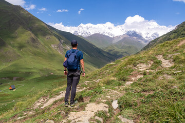 Naklejka na ściany i meble A male backpacker on a hiking trail to Chubedishi viewpoint. There is an amazing view on the Shkhara Glacier,near the village Ushguli the Greater Caucasus Mountain Range in Georgia, Svaneti Region