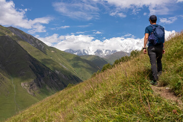 Naklejka na ściany i meble A male backpacker on a hiking trail to Chubedishi viewpoint. There is an amazing view on the Shkhara Glacier,near the village Ushguli the Greater Caucasus Mountain Range in Georgia, Svaneti Region