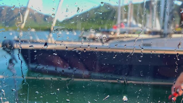 Close up view through wet glass of the crew of a huge boat washes a sailing yacht in clear sunny weather, it is preparing the luxury boat for the reception of guests