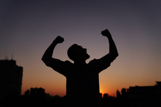Silhouette male dancing and feeling happy outdoor at sunset with urban background. Man pumping his fists in the air, victory businessman concept, dancing, raising hands and waving. High quality image