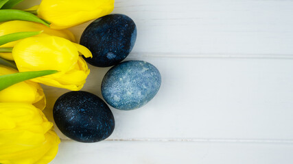 Beautiful yellow tulips and painted Easter eggs on a white wooden background. Congratulatory Easter background. Banner. Top view. Copy space.