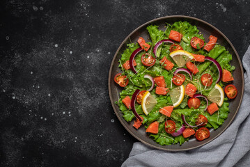 Salad with salmon and fresh vegetables on a black stone background. Top view, flat lay, copy space.