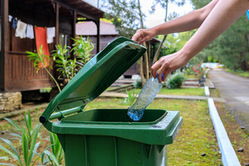 a human hand throws a plastic bottle into an open green garbage container