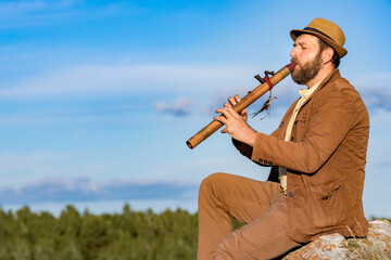music in nature, a man in a brown suit plays the flute - obrazy, fototapety, plakaty