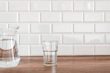 An empty glass and a jug of water stand in the kitchen
