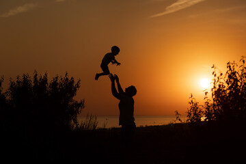 Silhouette of a man and a child against the sunset.Dad raises his son 
