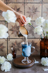 Blue tea with cream in a long stemmed glass. Hot morning drink on the table with white carnations