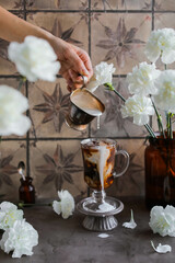 Cold coffee with cream. A woman's hand pours milk into strong iced coffee. Breakouts and splashes.