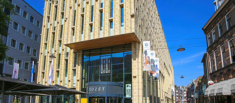 Arnhem (Rozet Centrum), Netherlands - July 9. 2021: View on entrance of modern architecture building in city center with outdoor restaurant cafe against blue summer sky