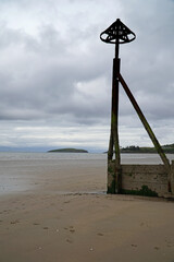 Wooden sea groyne or groin and marker on the beach at Abesrsoch, Wales, UK with Bardesy Island in the distance