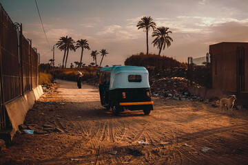 Black tuk tuk driving into the sunset in cairo suburbs in egypt, tiny motorbikes popular mode of...
