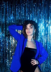  curly haired woman in blue jacket posing on sparkling disco background