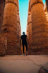 Vertical shot of man tourist walking around the massive pillars in luxor temple in egypt. Ancient egyptian pillars stand here after thousands of years, available for people to visit
