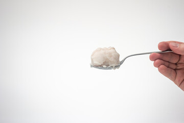 Pig fat or lard on a metal spoon held by Caucasian male hand. Close up studio shot, isolated on white background
