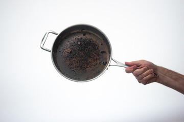 Dirty oily burnt metal frying pan or skillet held in hand by male hand. Close up studio shot,...