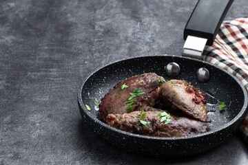 Fried chicken liver with herbs in a frying pan on gray background
