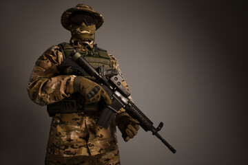 Fototapeta na wymiar Portrait of soldier in military camouflage uniform protected with helmet, body armor, holding machine gun desaturated on a gray background. Army. Sniper. Soldier shooting. Military Conflict Actions. 