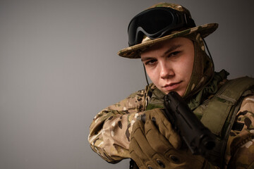 Portrait of  soldier in military camouflage uniform protected with helmet, body armor, Holding machine gun desaturated on a gray background. Military Conflict Actions. Man In camouflage.