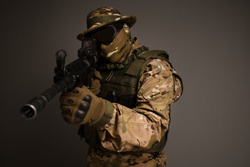 Portrait of soldier in military camouflage uniform protected with helmet, body armor, holding machine gun desaturated on a gray background. Army. Sniper. Soldier shooting. Military Conflict Actions. 